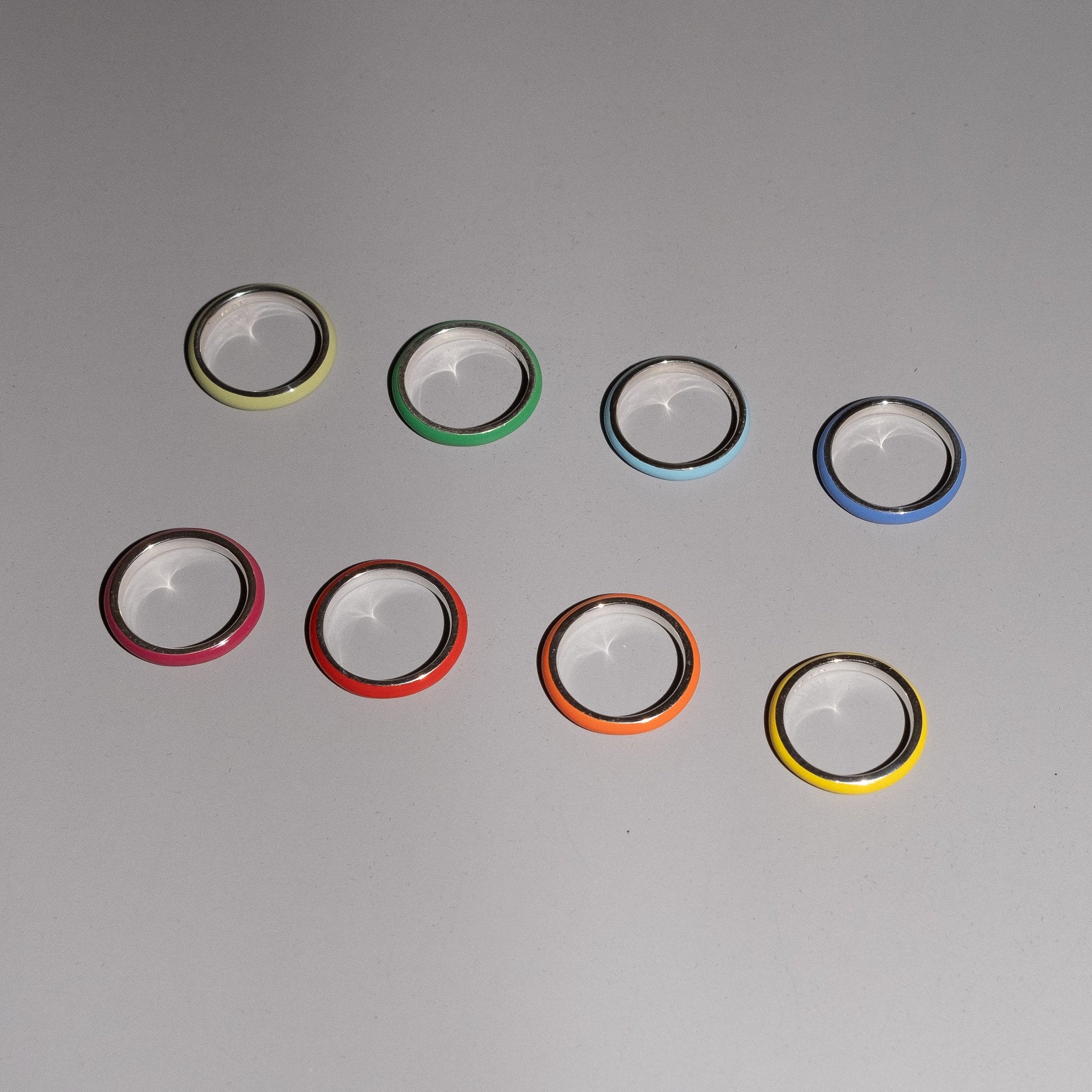 Seven clear circular lens protectors or camera lens covers with colored outer rims in yellow, green, light blue, dark blue, pink, red, orange, and yellow, arranged on a neutral gray background.