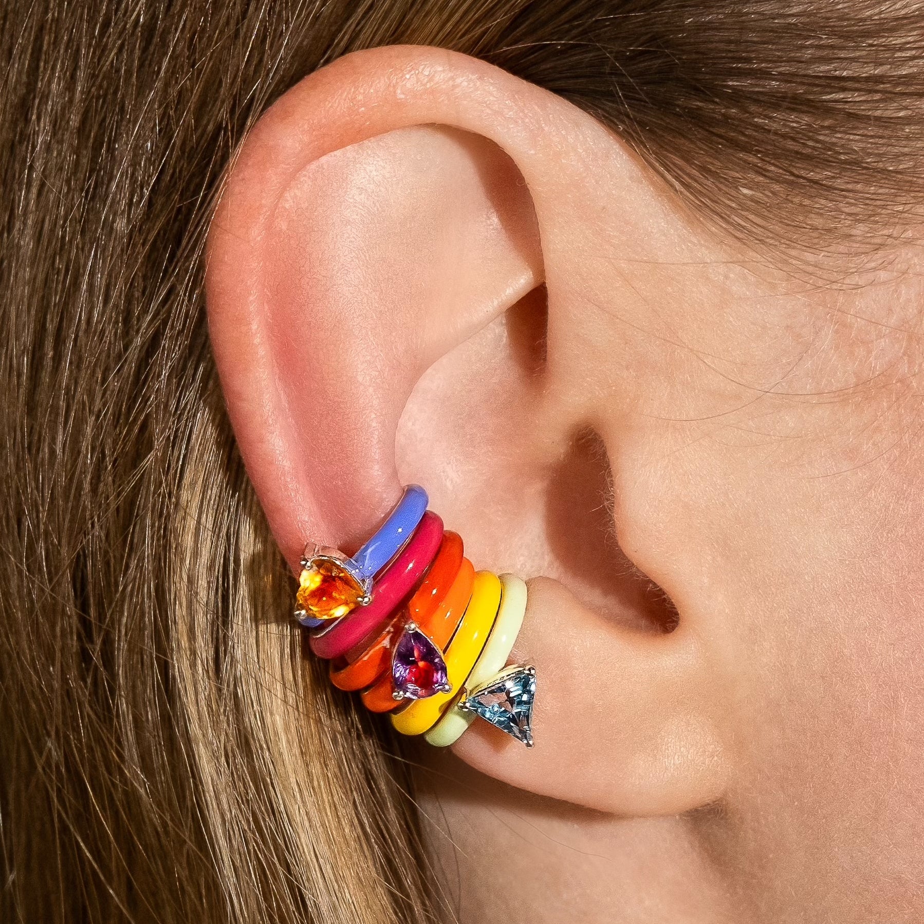 Close-up of an ear wearing a colorful earring with gemstones.