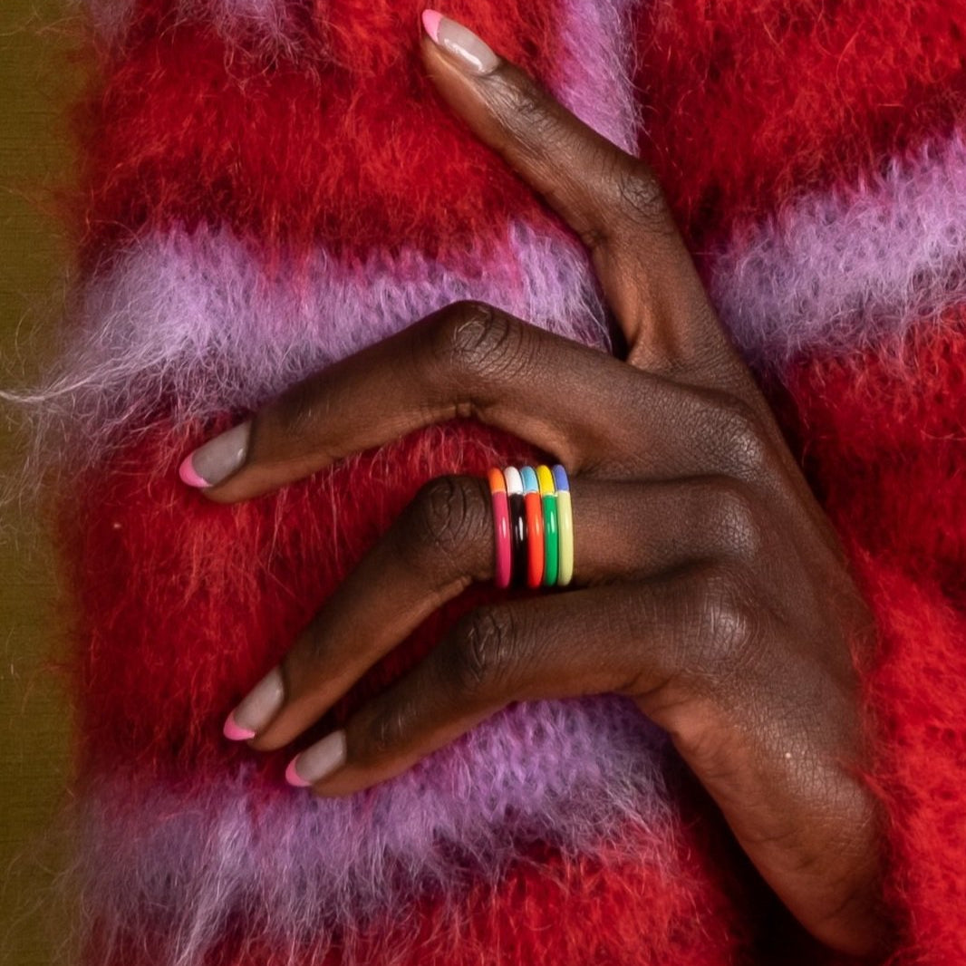 A close-up of a hand wearing a stack of four colorful rings, resting on a textured, fuzzy red and pink blanket.
