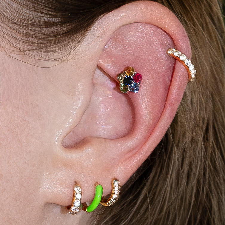 Close-up of an ear with multiple earrings including a colorful flower-shaped one.