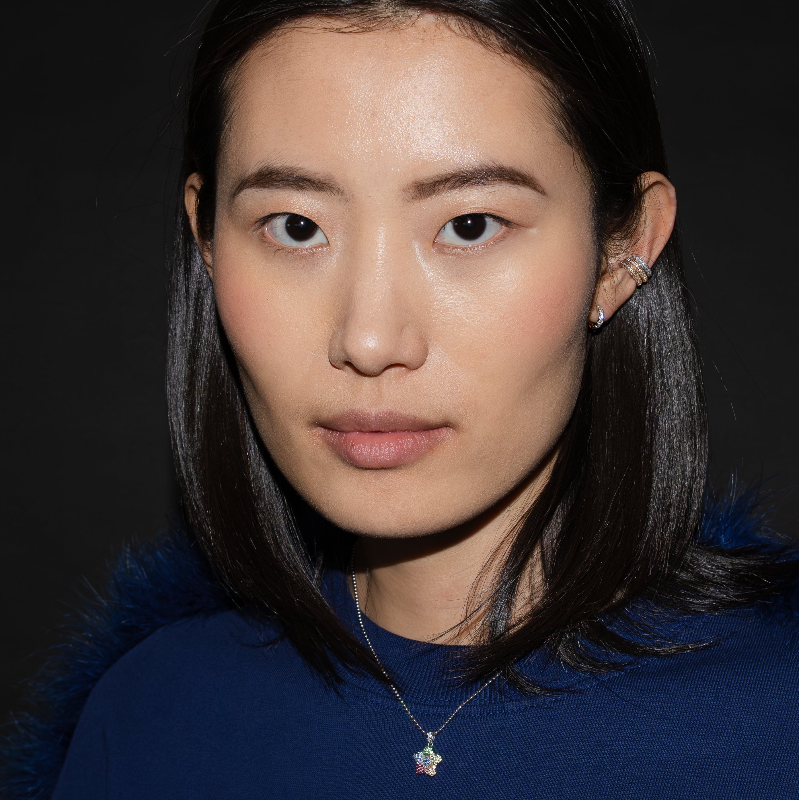 Person with dark hair and a neutral expression against a dark background