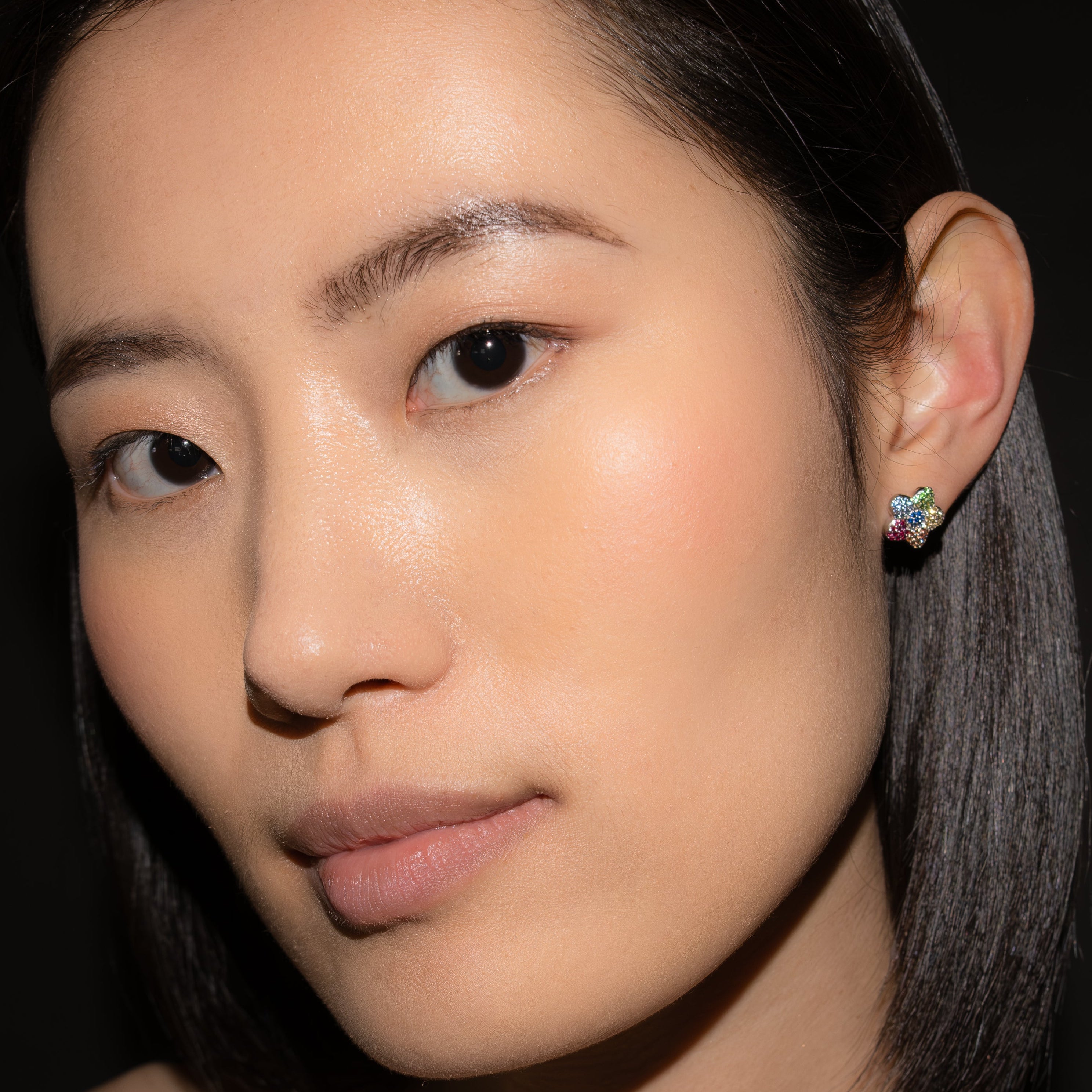Close-up of a person wearing a floral earring against a dark background.