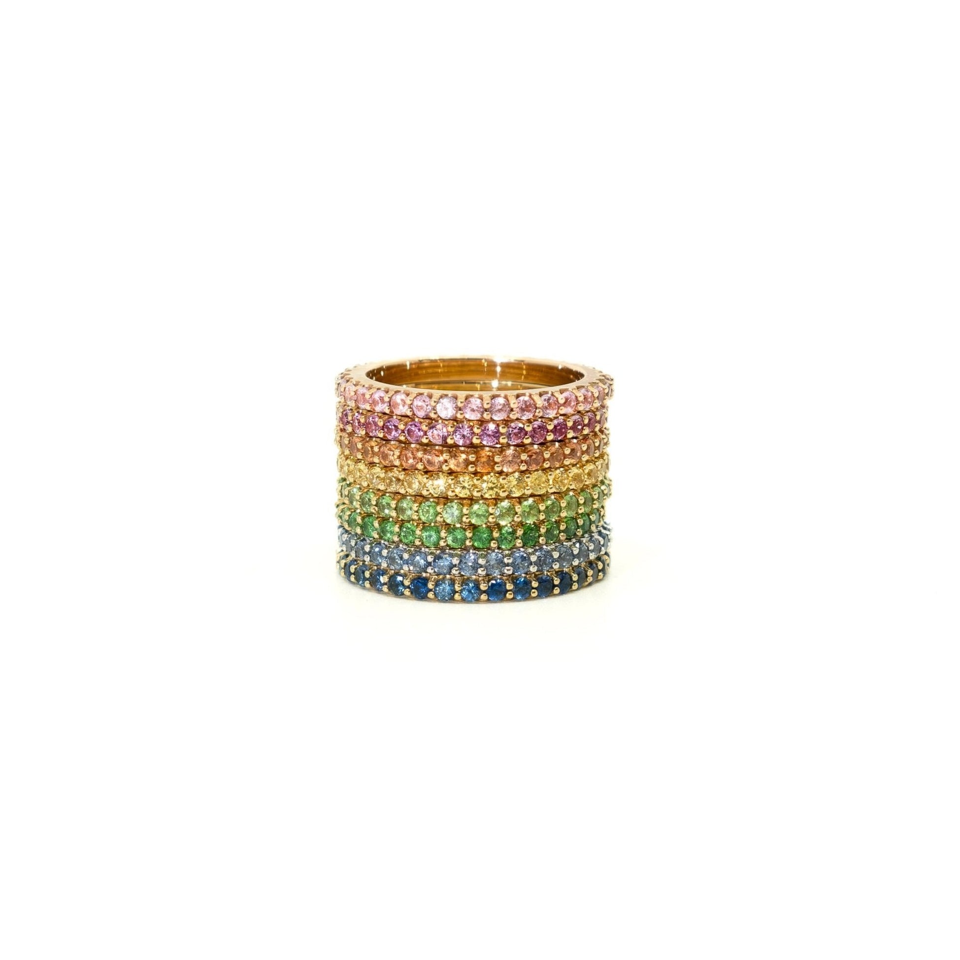 A stack of six wide rings set with rainbow-colored gemstones in a gold-tone setting, displayed on a clean white background.