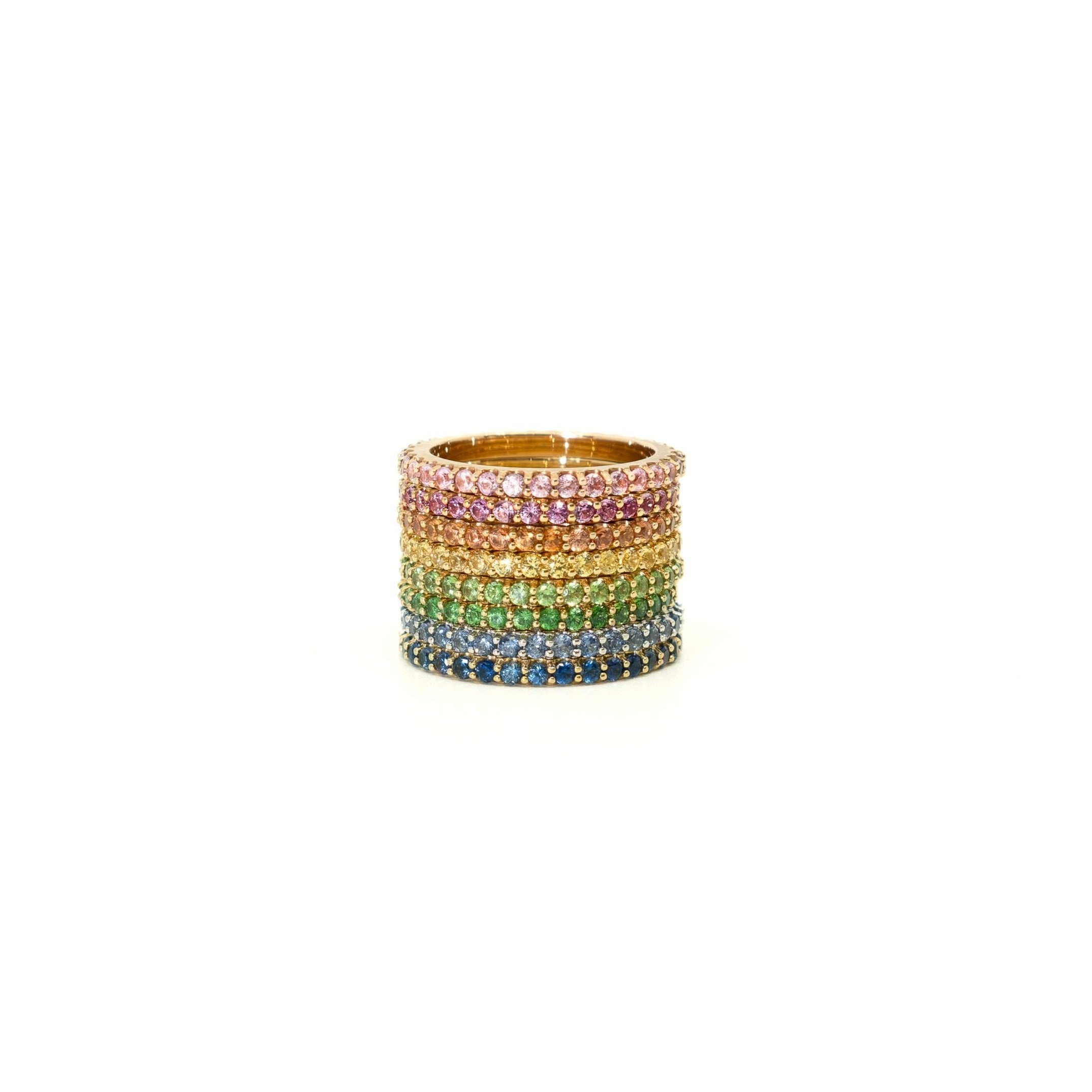 A stack of six wide rings set with rainbow-colored gemstones in a gold-tone setting, displayed on a clean white background.