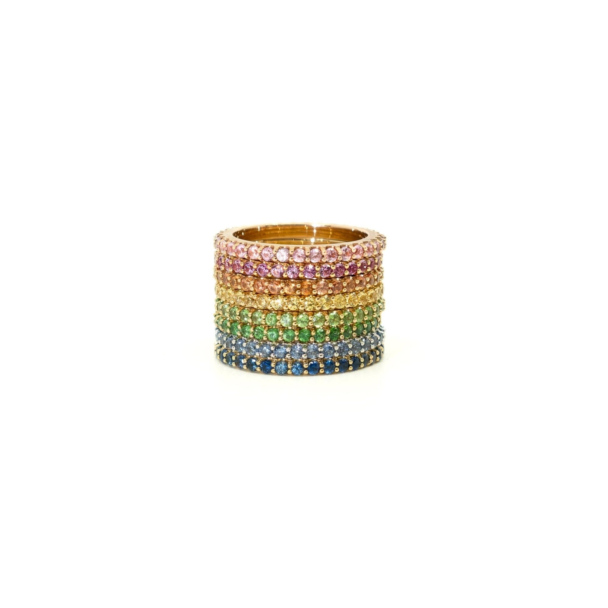A stack of six wide rings set with rainbow-colored gemstones in a gold-tone setting, displayed on a clean white background.
