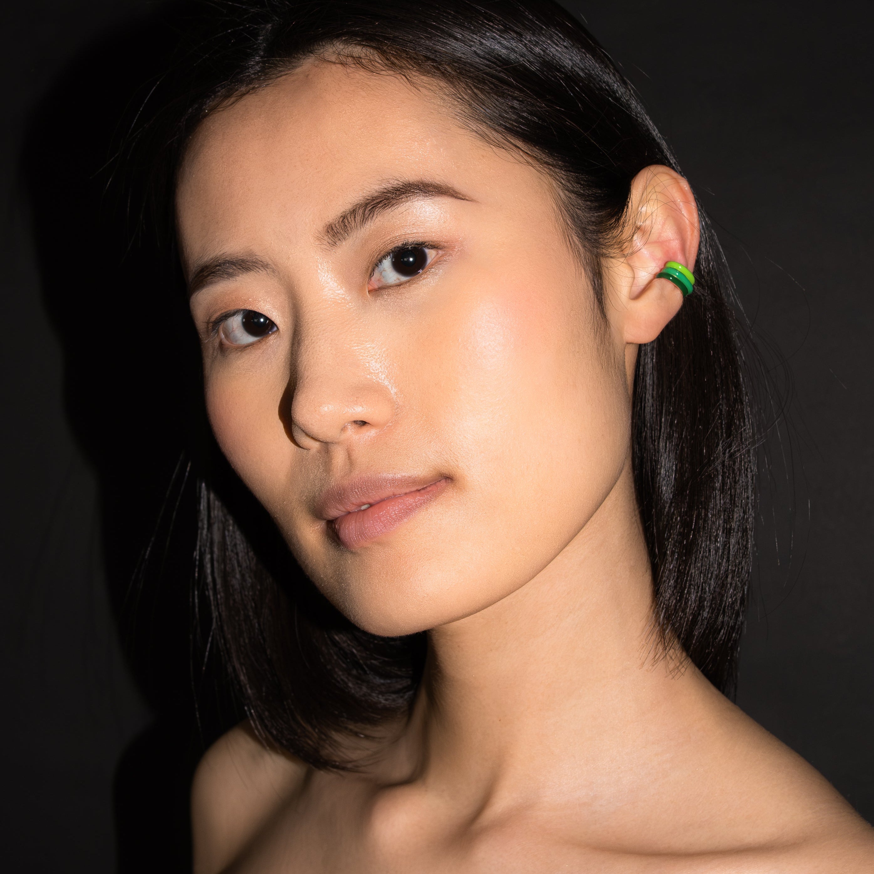 Woman with a green earring against a dark background