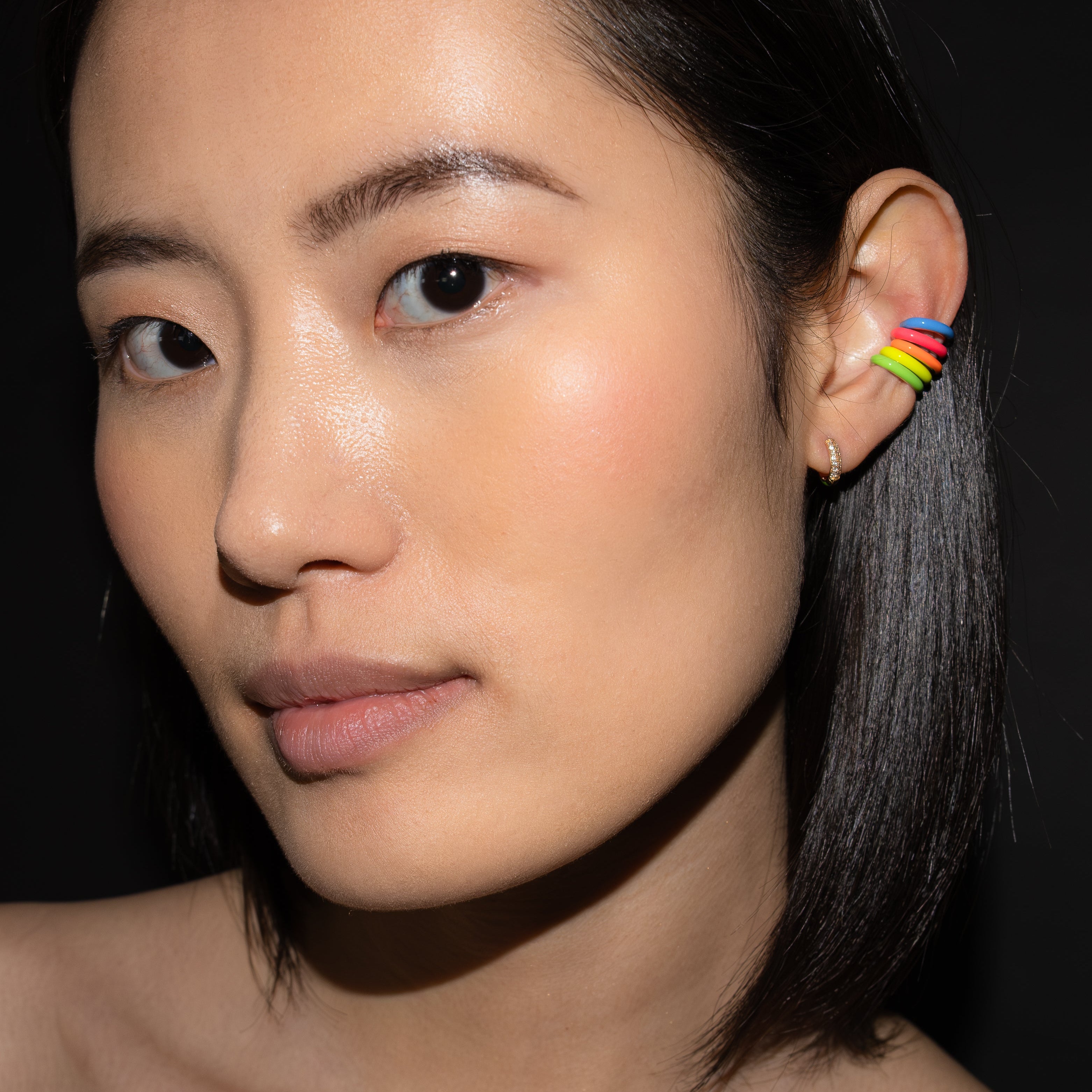 Person wearing a rainbow set of five ear cuff earrings against a dark background.