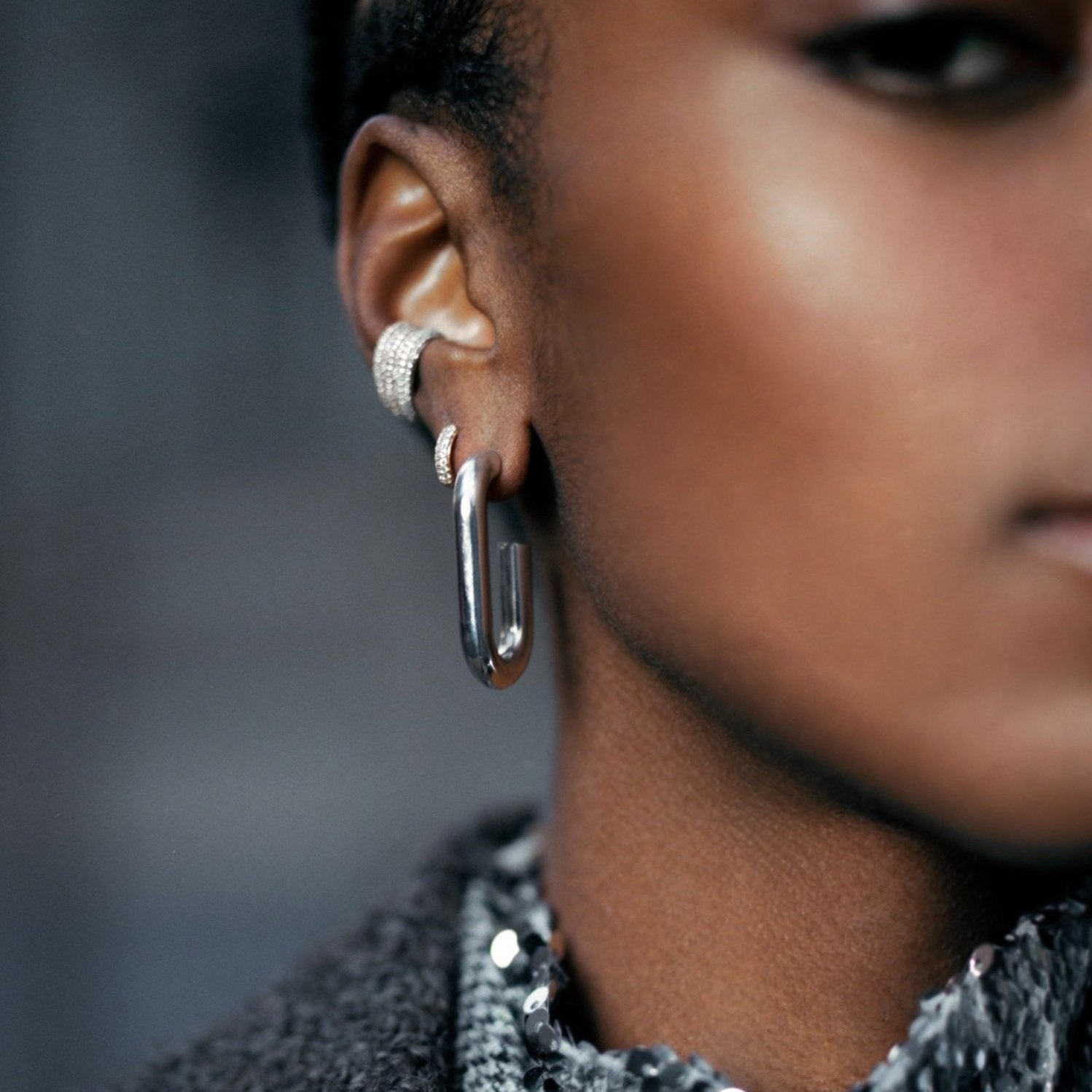 A close-up of a person wearing a pair of silver-toned hoop earrings, with one larger polished hoop and one textured silver hoop, against a dark blurred background.