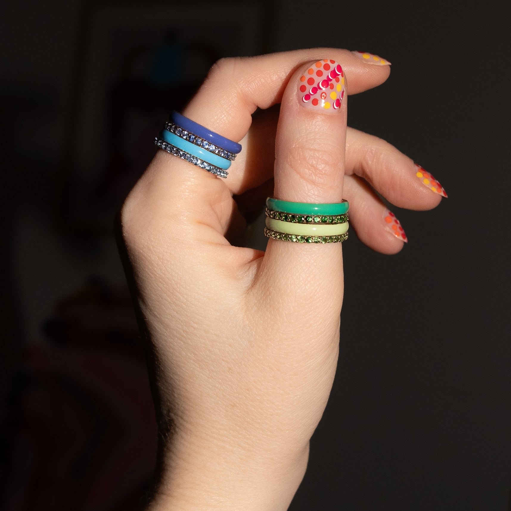 Hand with colorful nail polish and multiple rings on a dark background