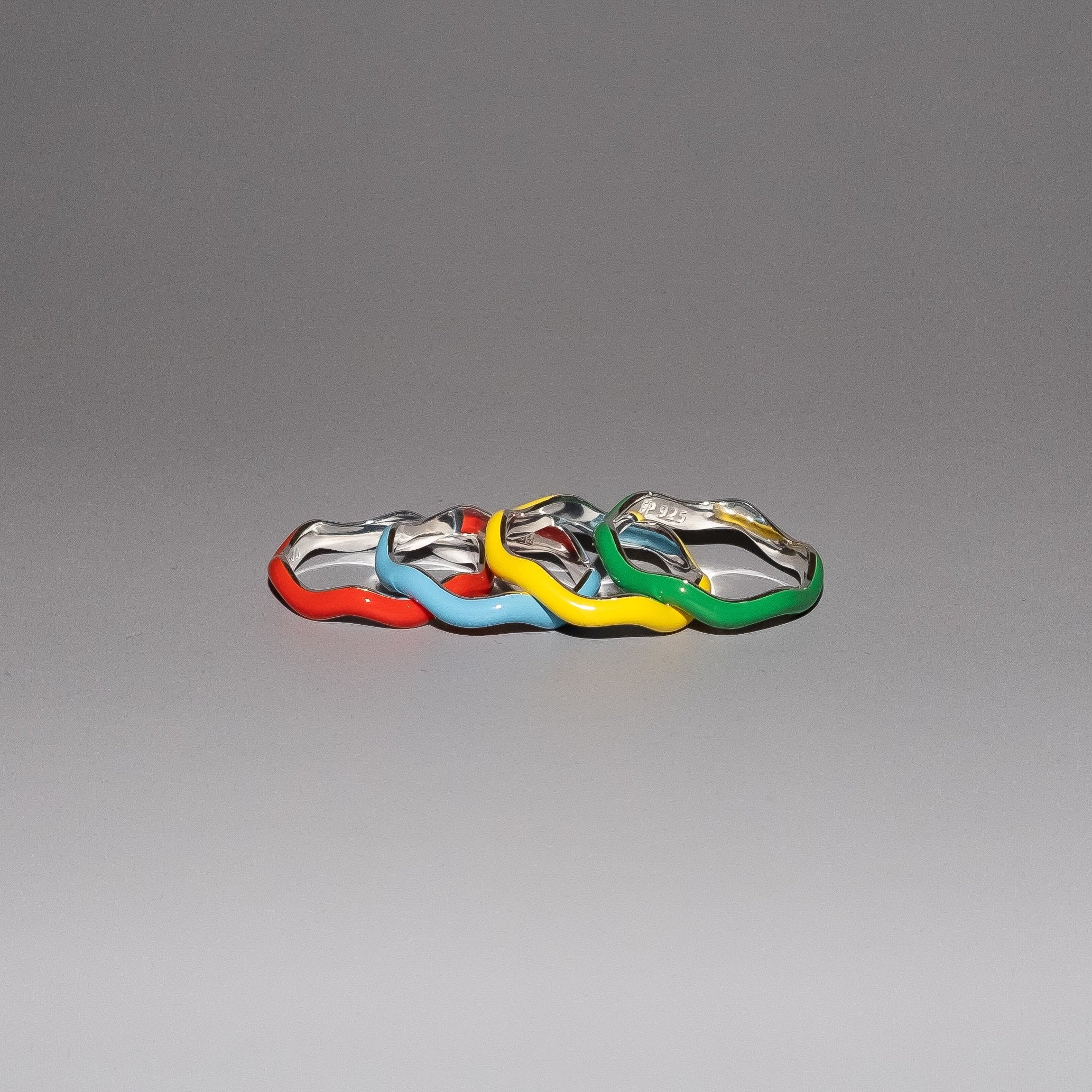 Four small, colorful, metallic car-shaped charms or beads in red, light blue, yellow, and green, arranged in a row on a smooth gray gradient background.