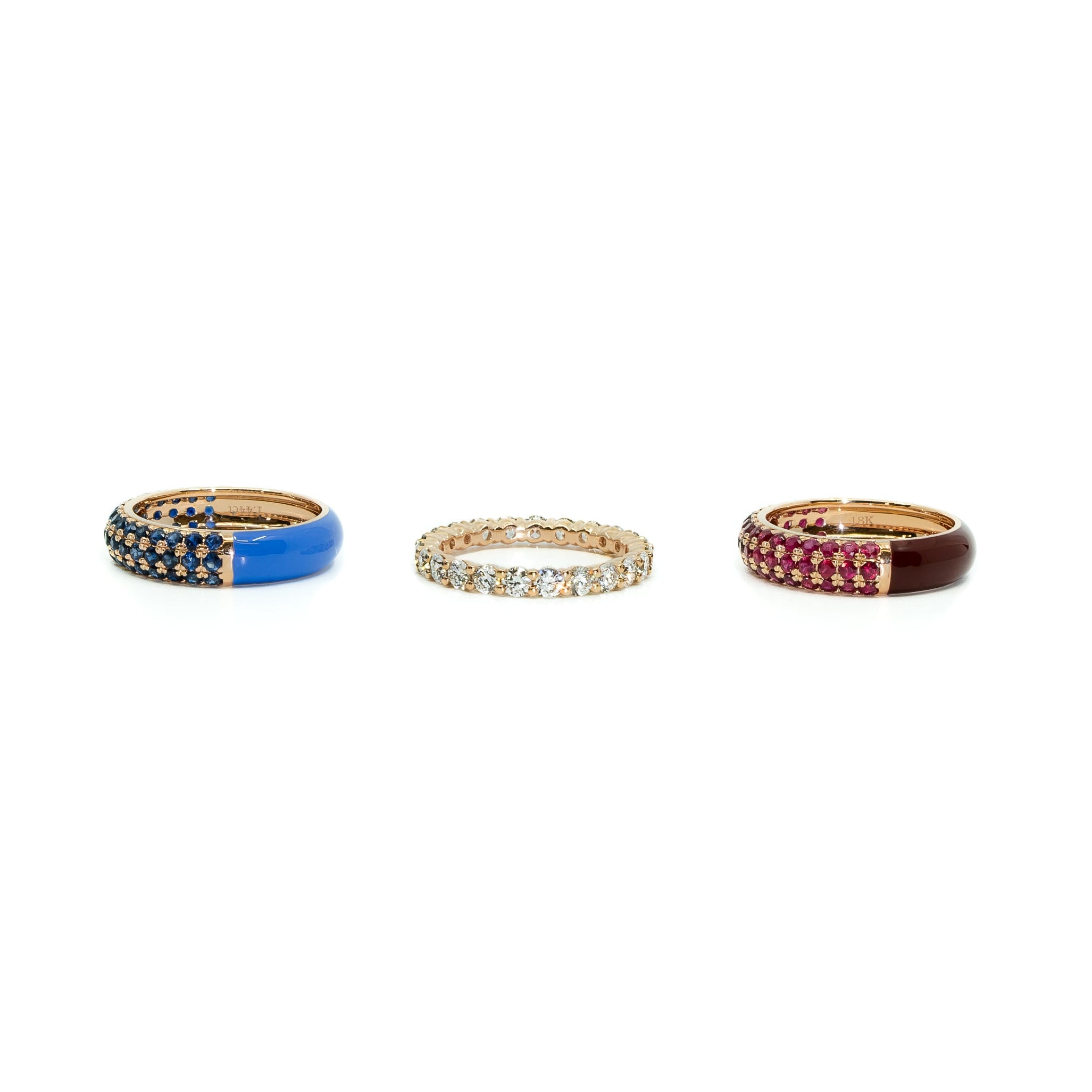 Three gold rings displayed horizontally on a white background. The left ring features a vibrant blue enamel band with pavé-set dark blue stones.