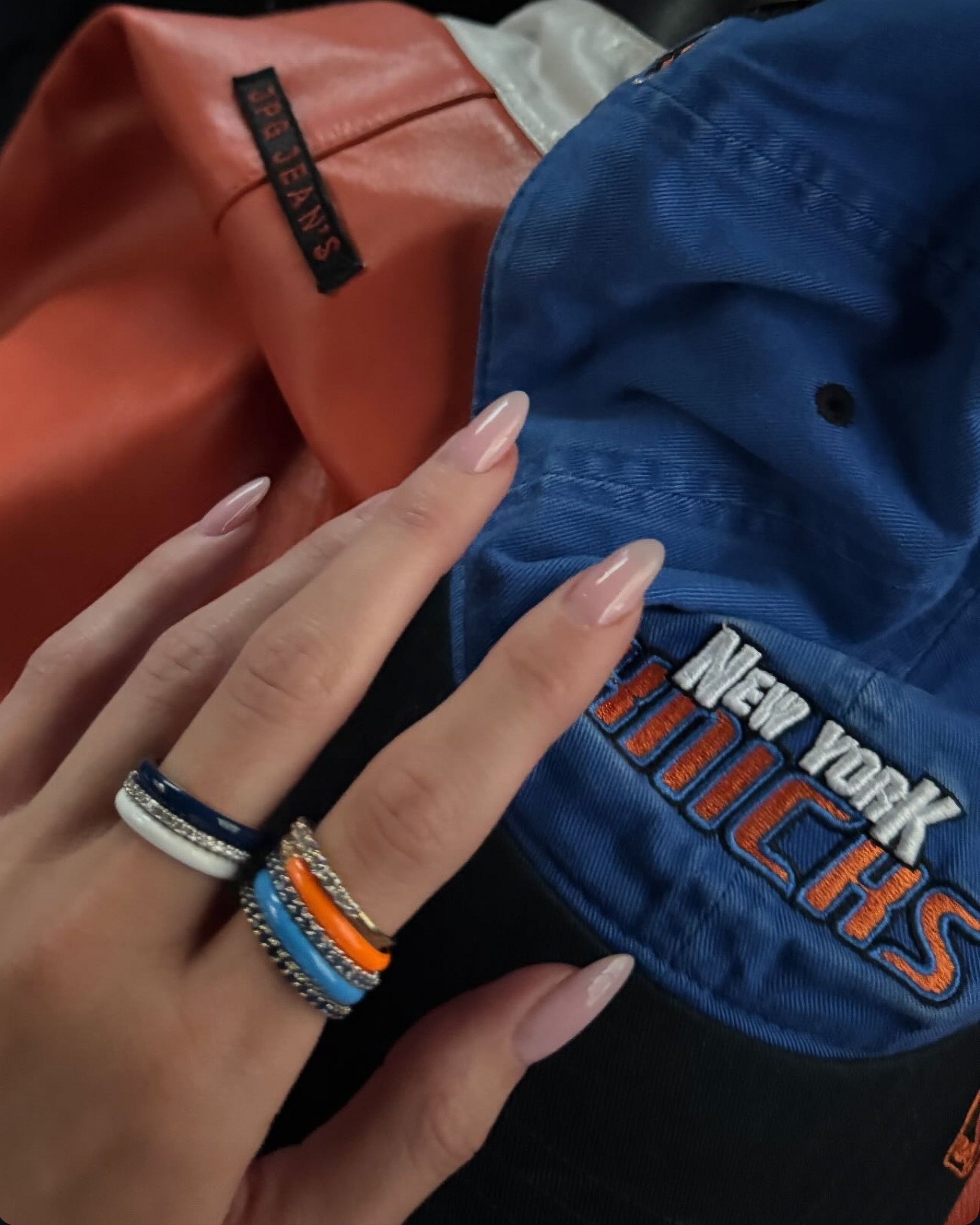 Close-up of Kylie Jenner's hand with multiple rings on a blue cap.