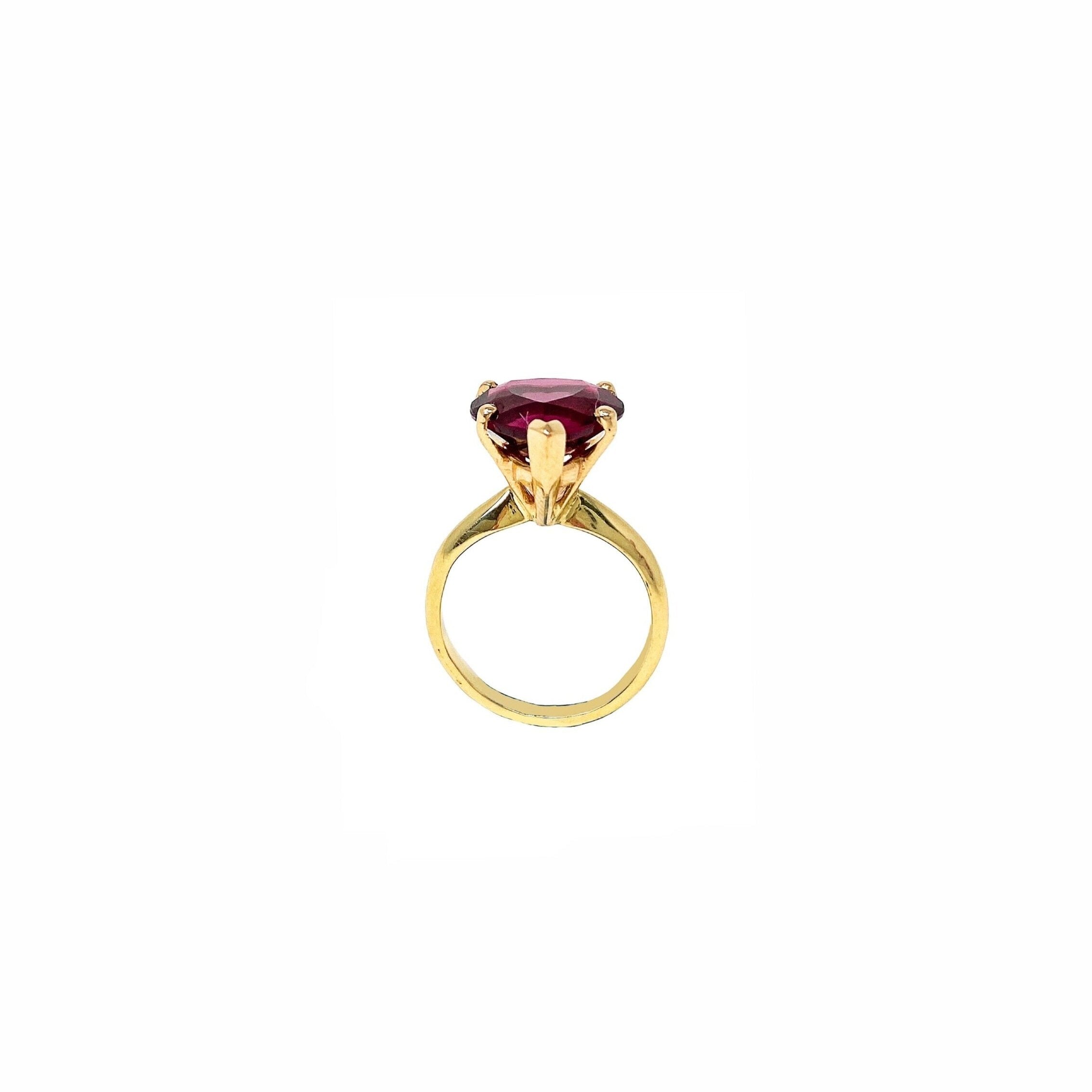 A yellow gold ring featuring a cushion-cut dark red gemstone in a prong setting, shown against a plain white background.