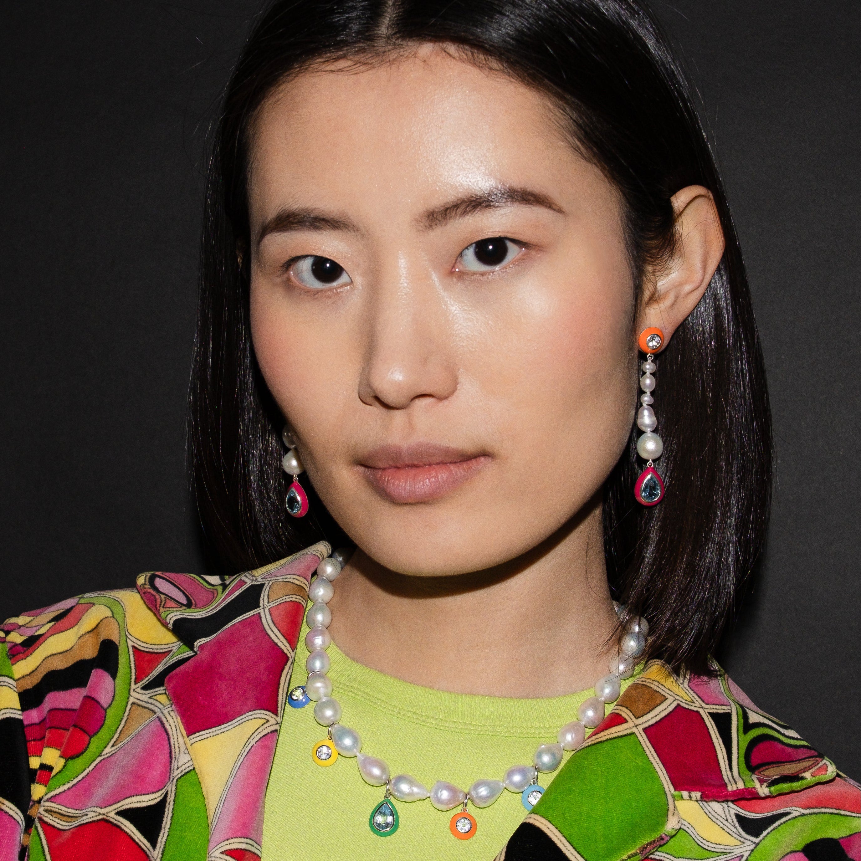 Woman wearing a colorful patterned garment with a pearl necklace against a dark background