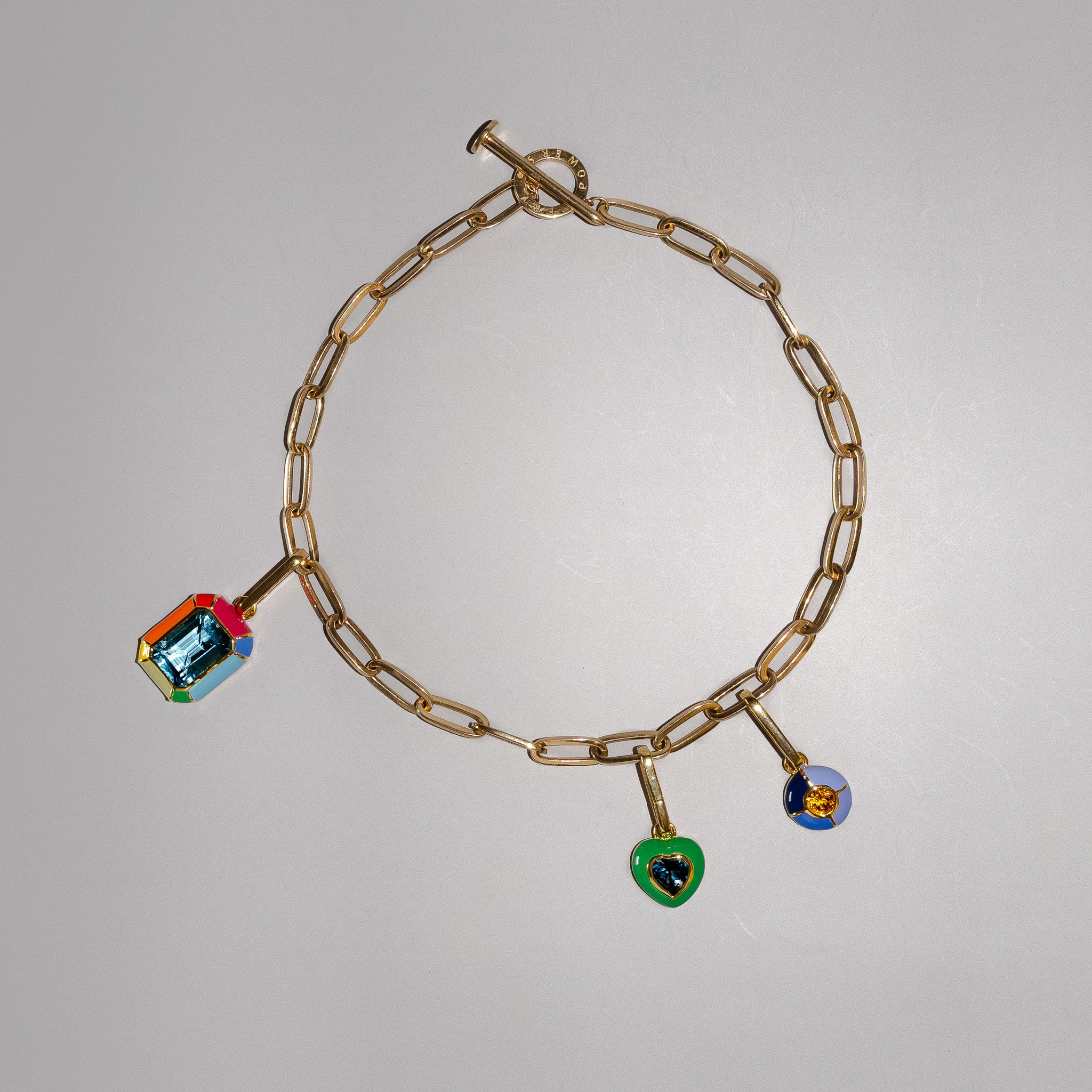 Gold chain necklace with three charm. A rainbow charm with blue topaz gemstone, a green enamel heart charm with london blue topaz gemstone, and a violet ombre round charm with an orange citrine gemstone.
