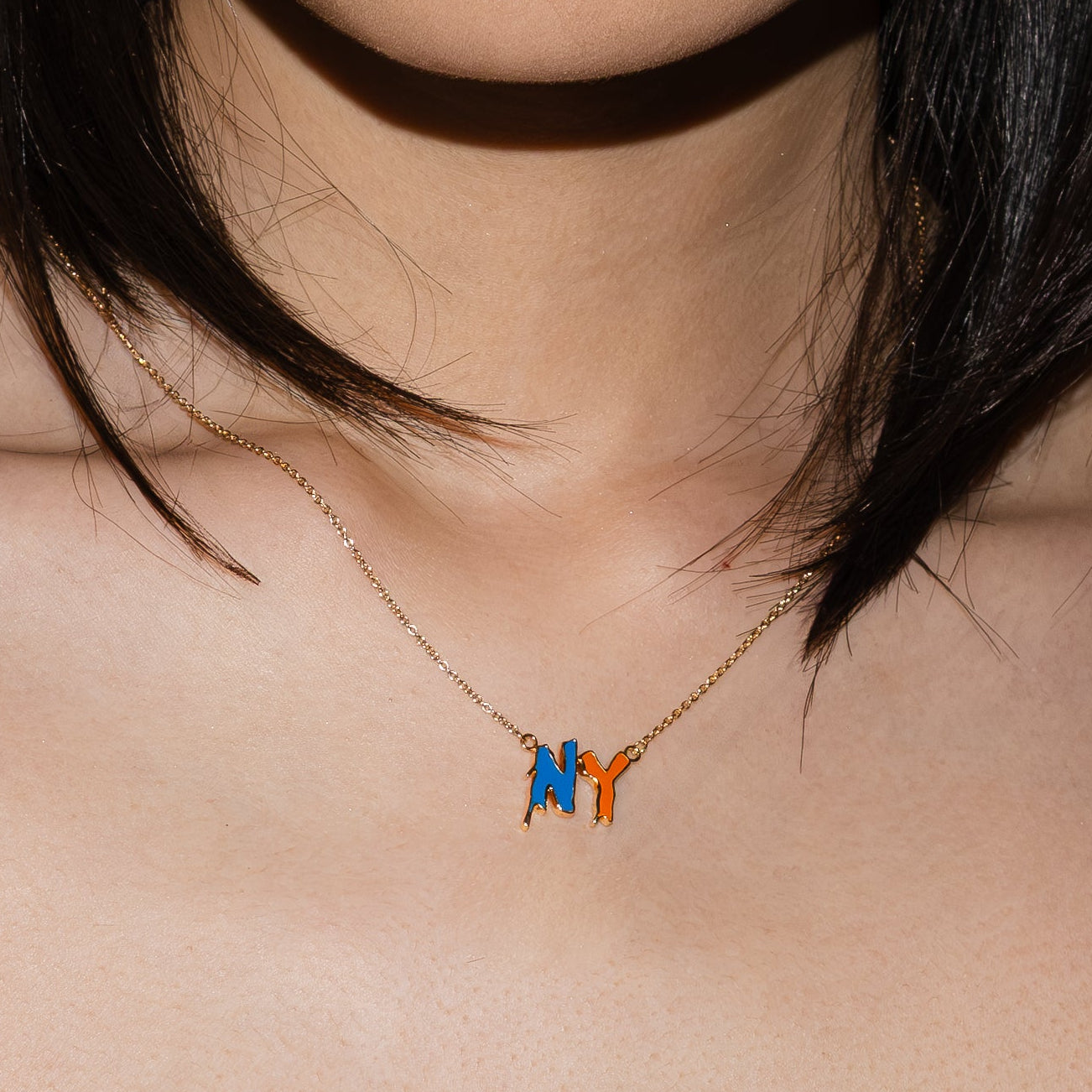 Close-up of a necklace with a 'NY' pendant on a person's neck.