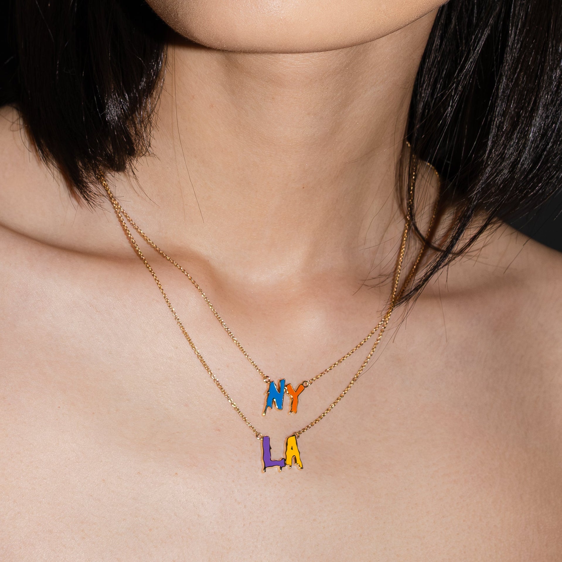 Close-up of a person wearing a gold necklace with colorful letter pendants.