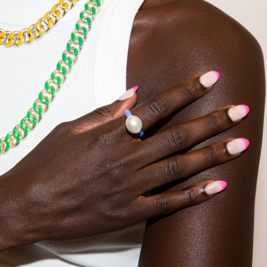 Woman's hand with pink manicure wearing a violet enamel ring with medium sized baroque pearl on top.