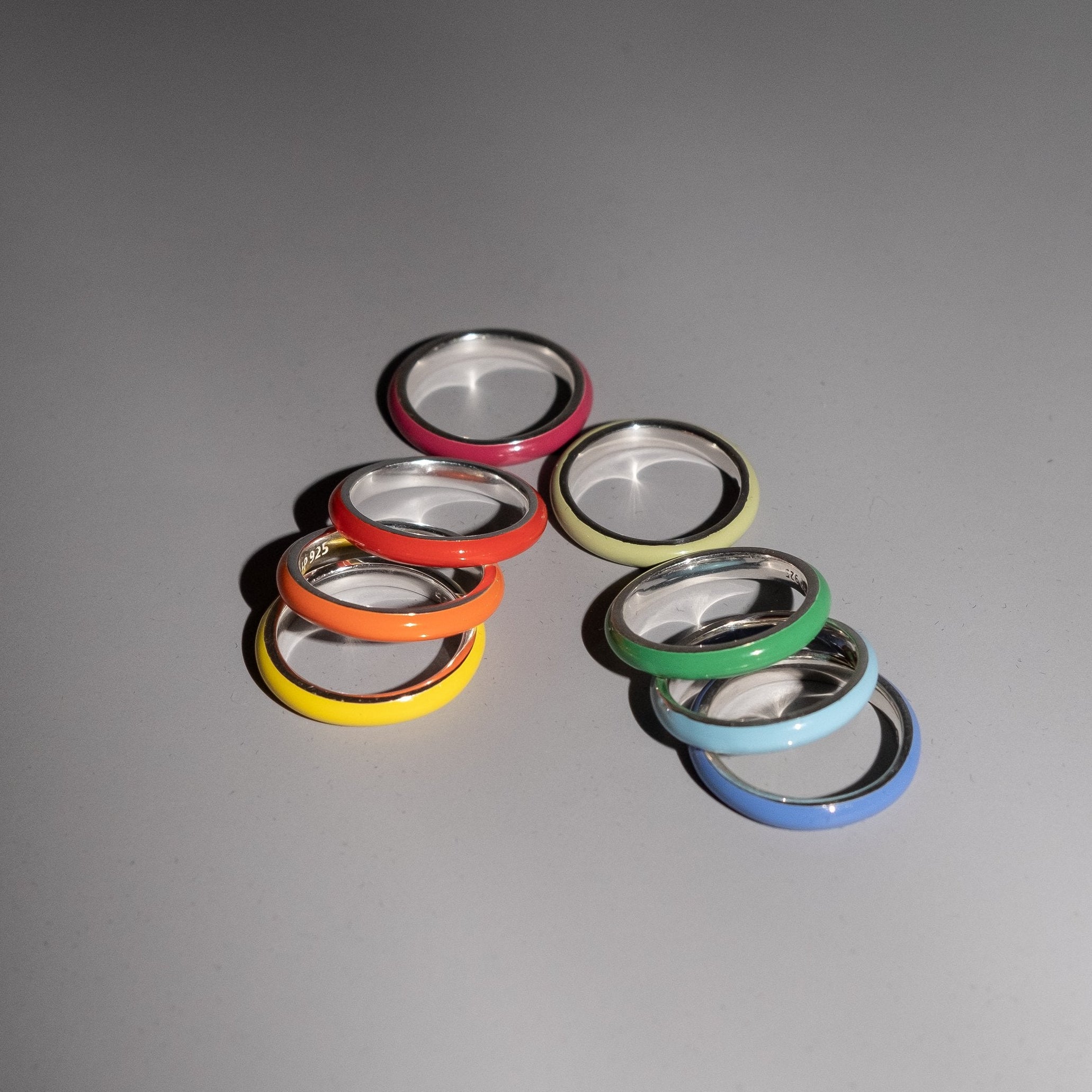 Eight colorful ring bands with silver-toned metal interiors, arranged in two small groups on a smooth gray surface.