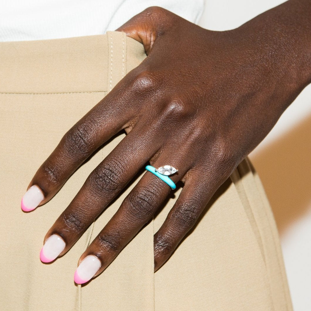 A close-up of a person's hand resting on beige trousers, wearing a silver ring with a turquoise blue stone.