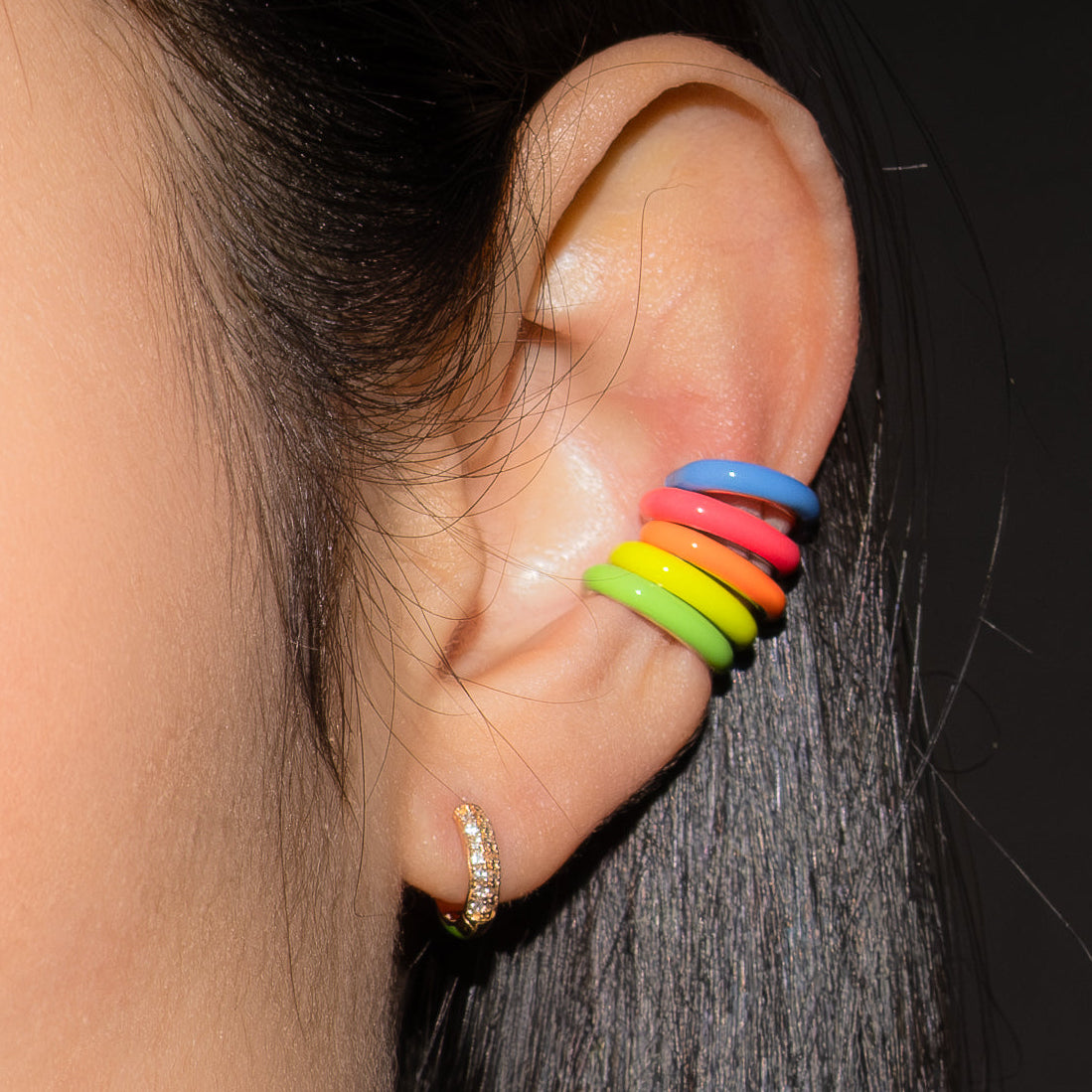 Close-up of an ear with a rainbow-colored earring against a dark background.