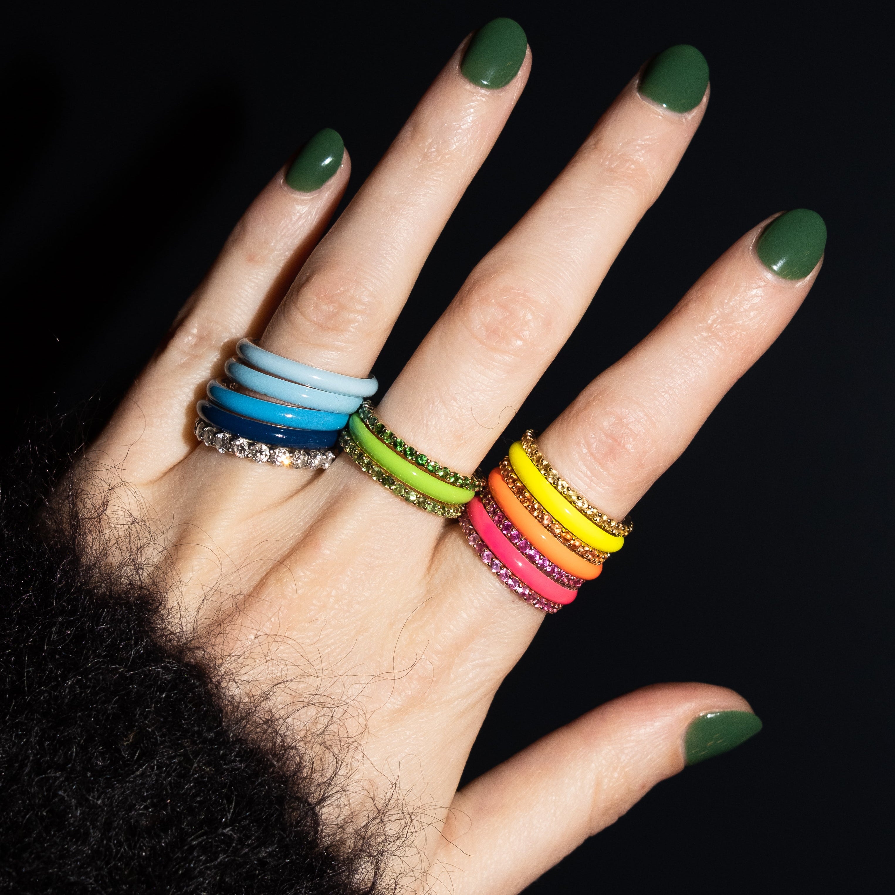 Hand with green nail polish wearing colorful rings on a black background