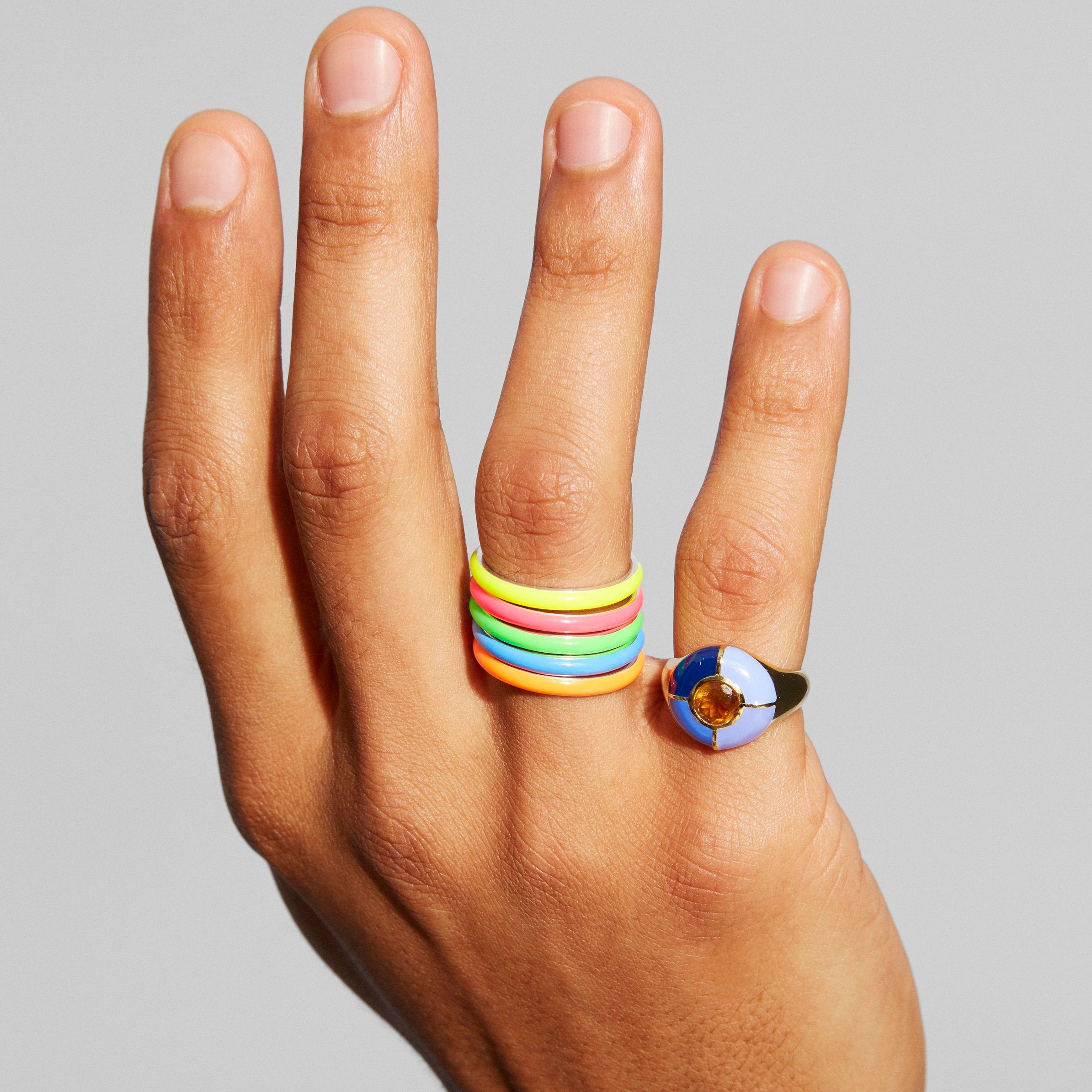 A hand wearing a stack of four colorful rings and a ring with a small flag of Argentina emblem, shown against a plain gray background.