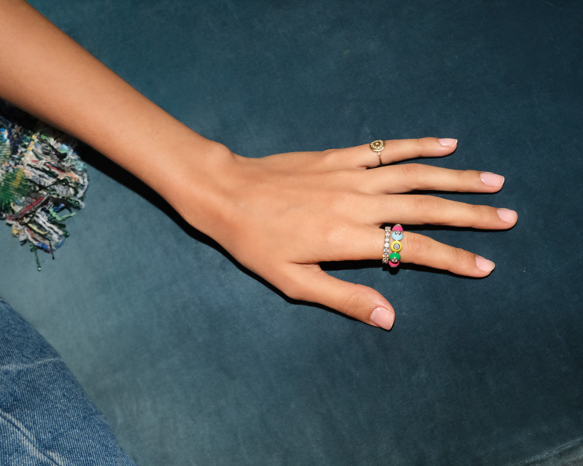 Hand wearing POWERS POP enamel and gemstone rings against a dark teal background.