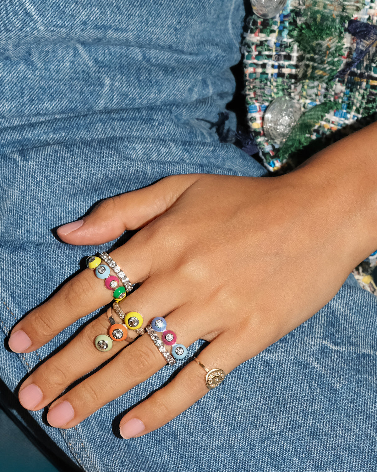 Hand wearing colorful POWERS POP enamel and gemstone rings against blue denim.