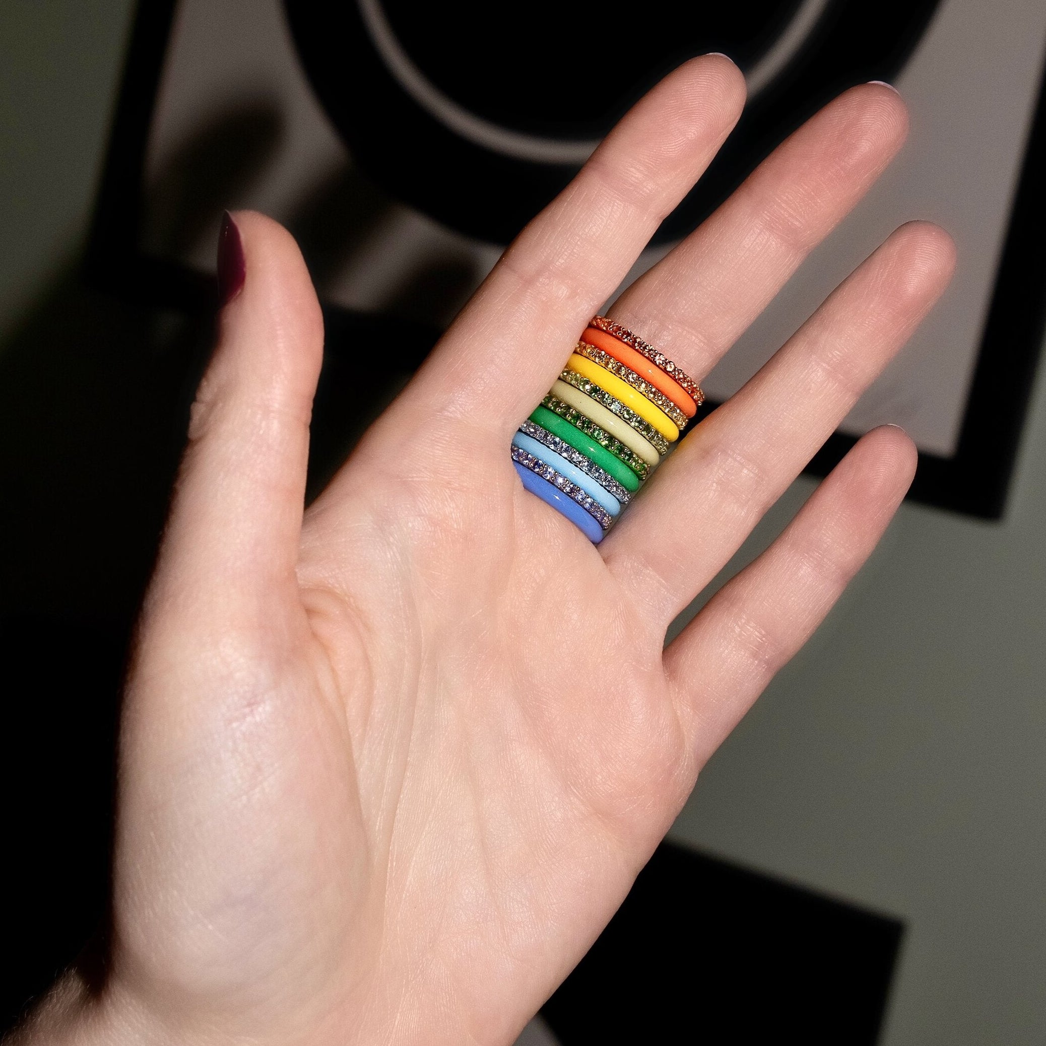 Hand wearing a rainbow ring with a black background featuring smiley face designs.