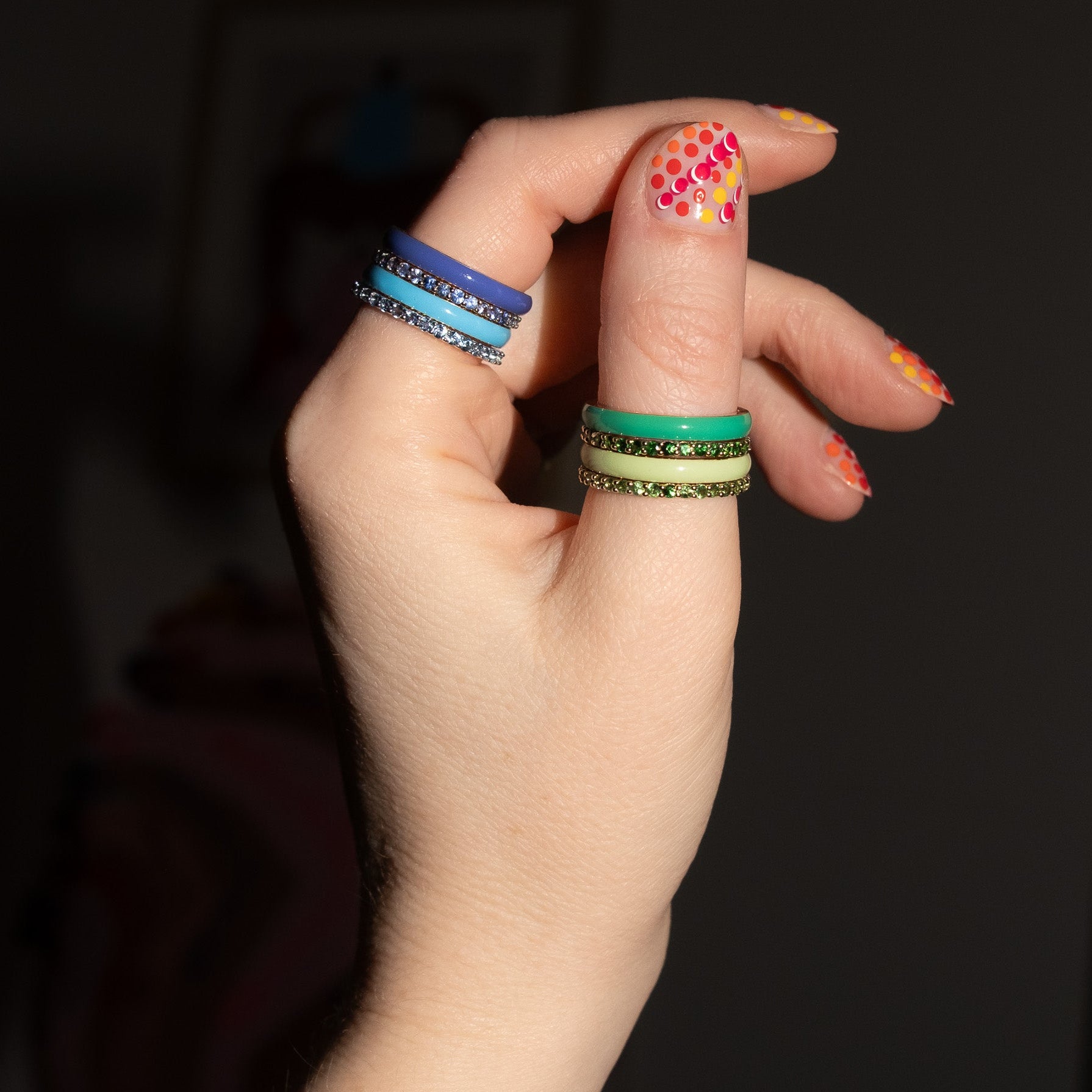 Hand with colorful nail polish and multiple rings on a dark background