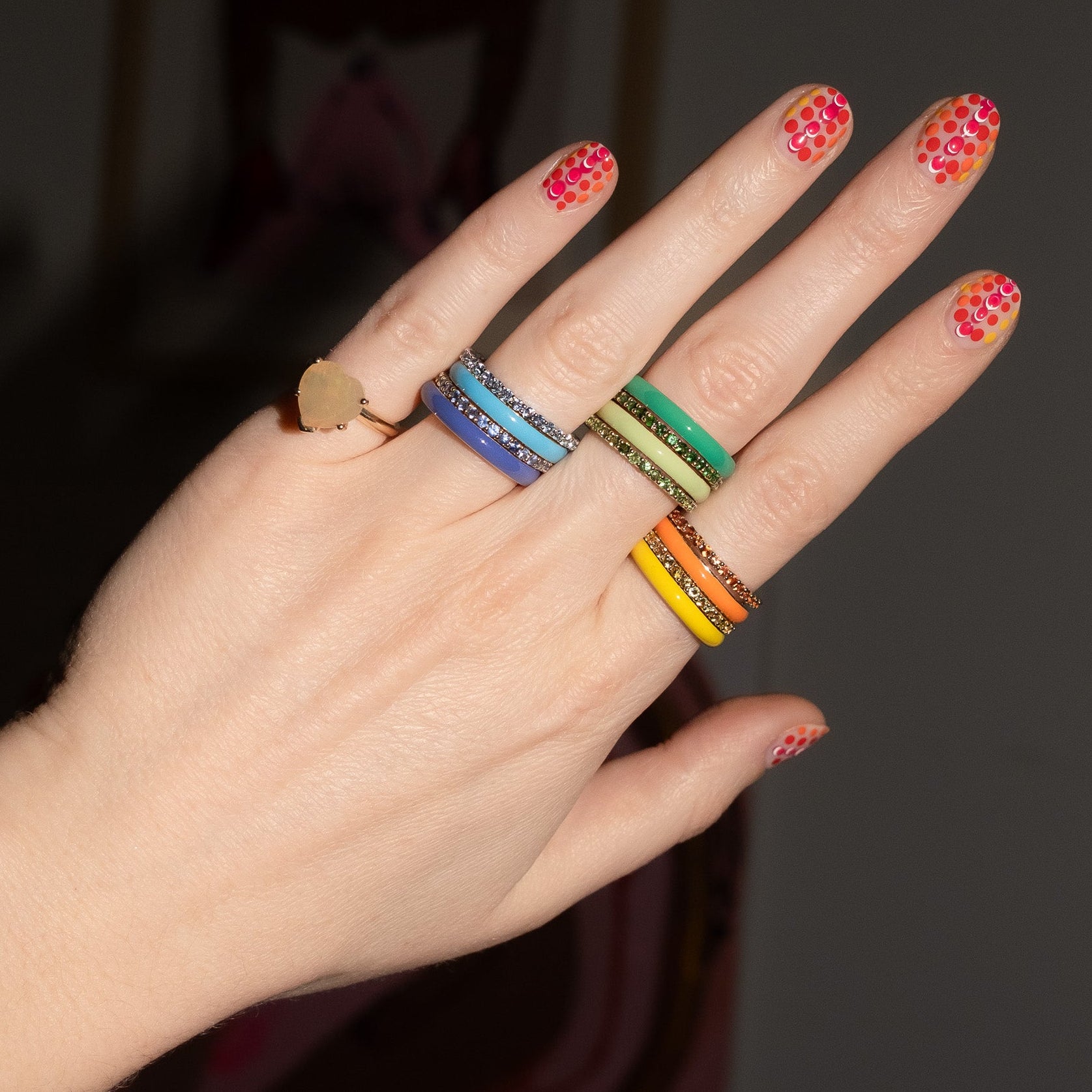 Hand wearing colorful rings with a dark background