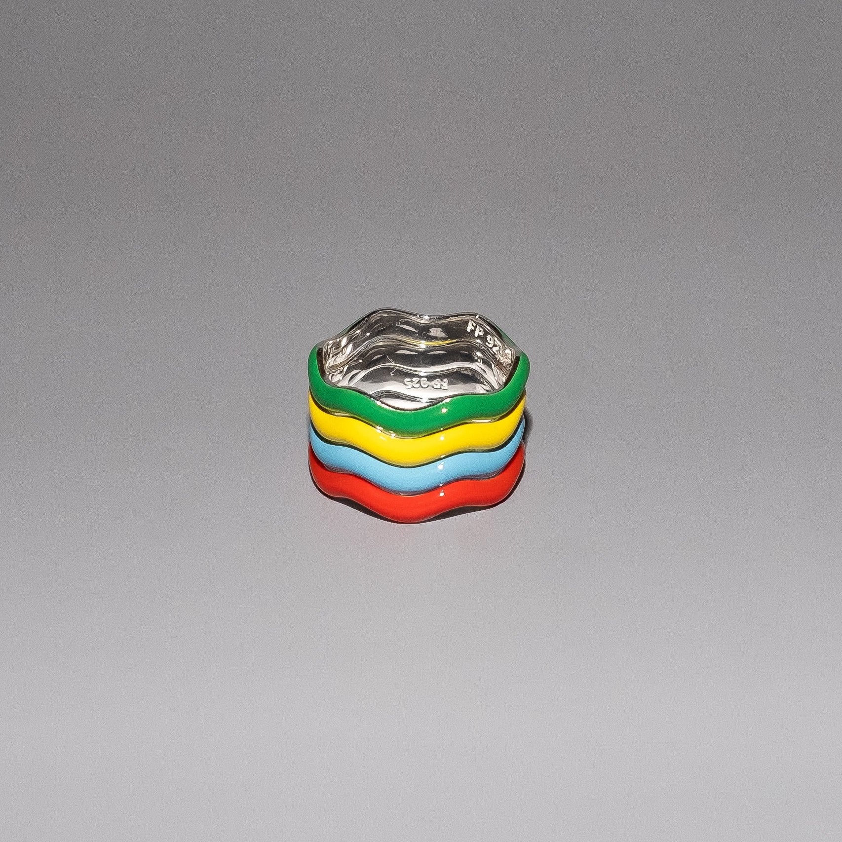 A set of four colorful enamel stacking rings on a grey background, with each ring featuring a different primary color.
